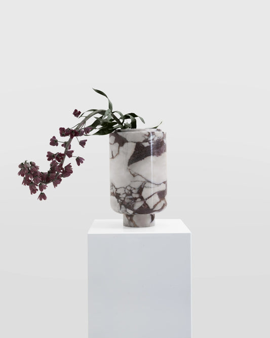 Kata Vase from premium Kütahya Viola marble with dried flowers on a white pedestal against a light gray background