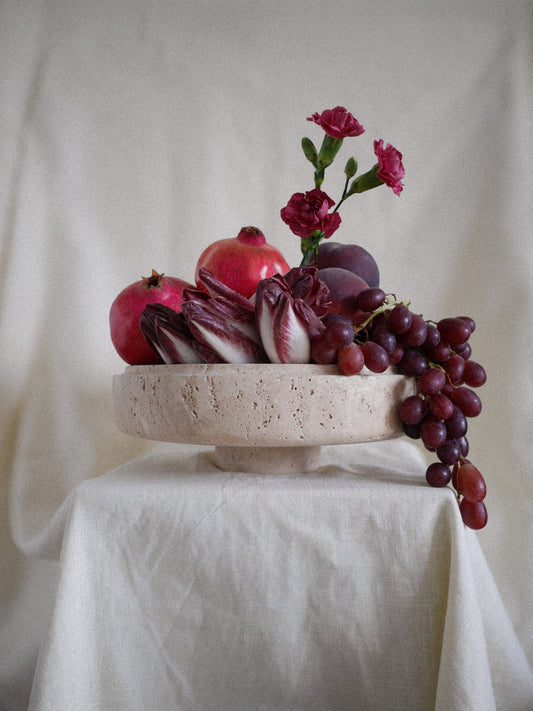 Bruna Bowl styled as a centerpiece, filled with grapes, pomegranates, radicchio, and pink flowers, emphasizing its elegant and functional design.