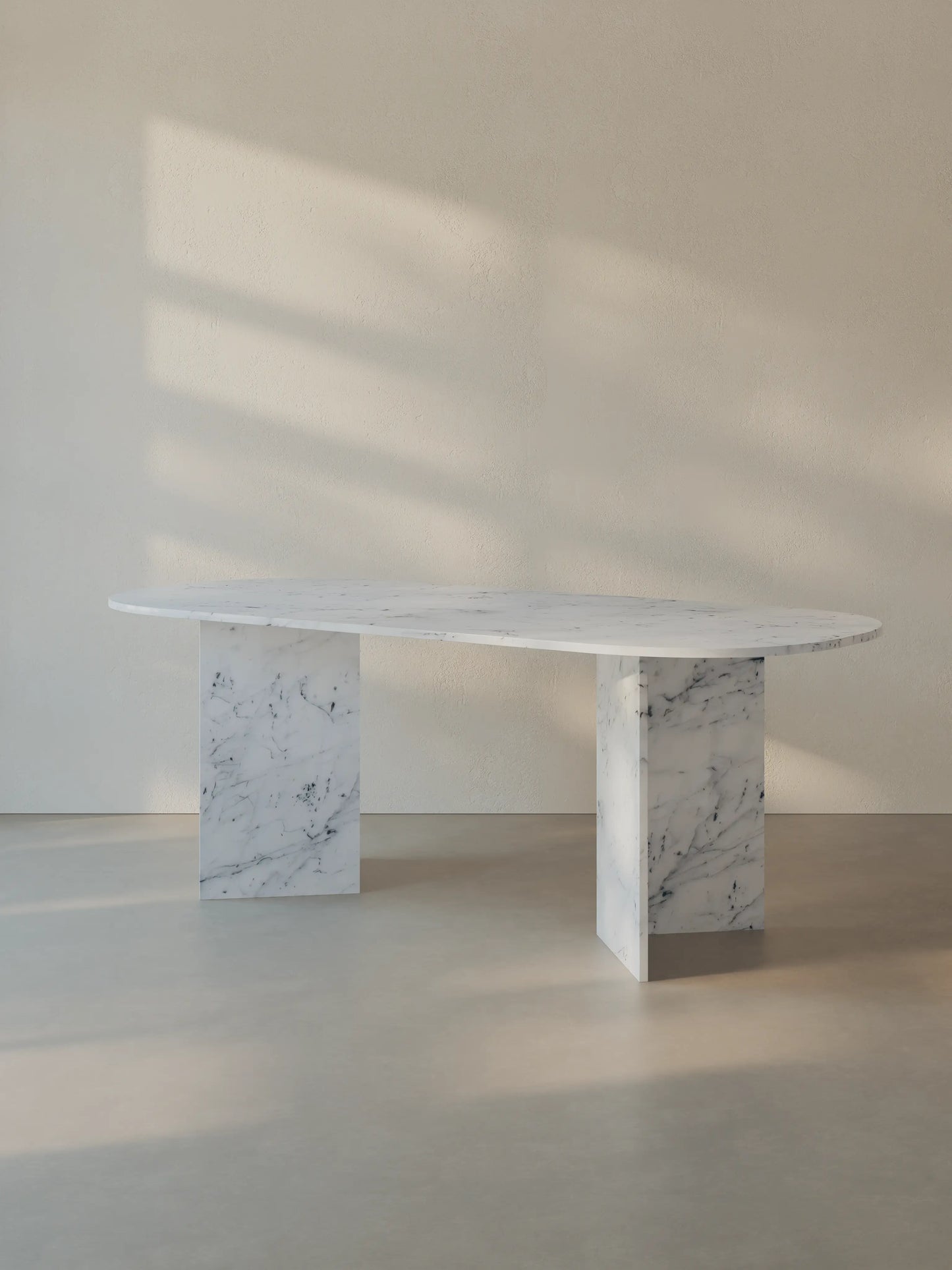 Sienae Dining Table in Carrara Bianco marble with oval-edged tabletop, shown from a slight angle highlighting the V-shaped base