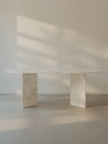 Sienae Dining Table in Navona Travertine with oval-edged tabletop and sculptural V-shaped base, shown from the front