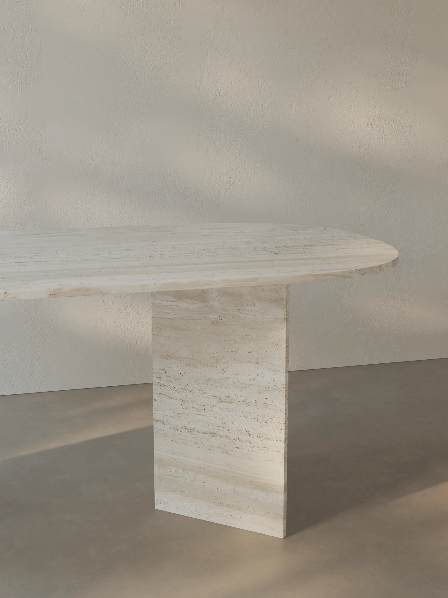 Side view of the Sienae Dining Table in Navona Travertine showing the sculptural V-shaped base