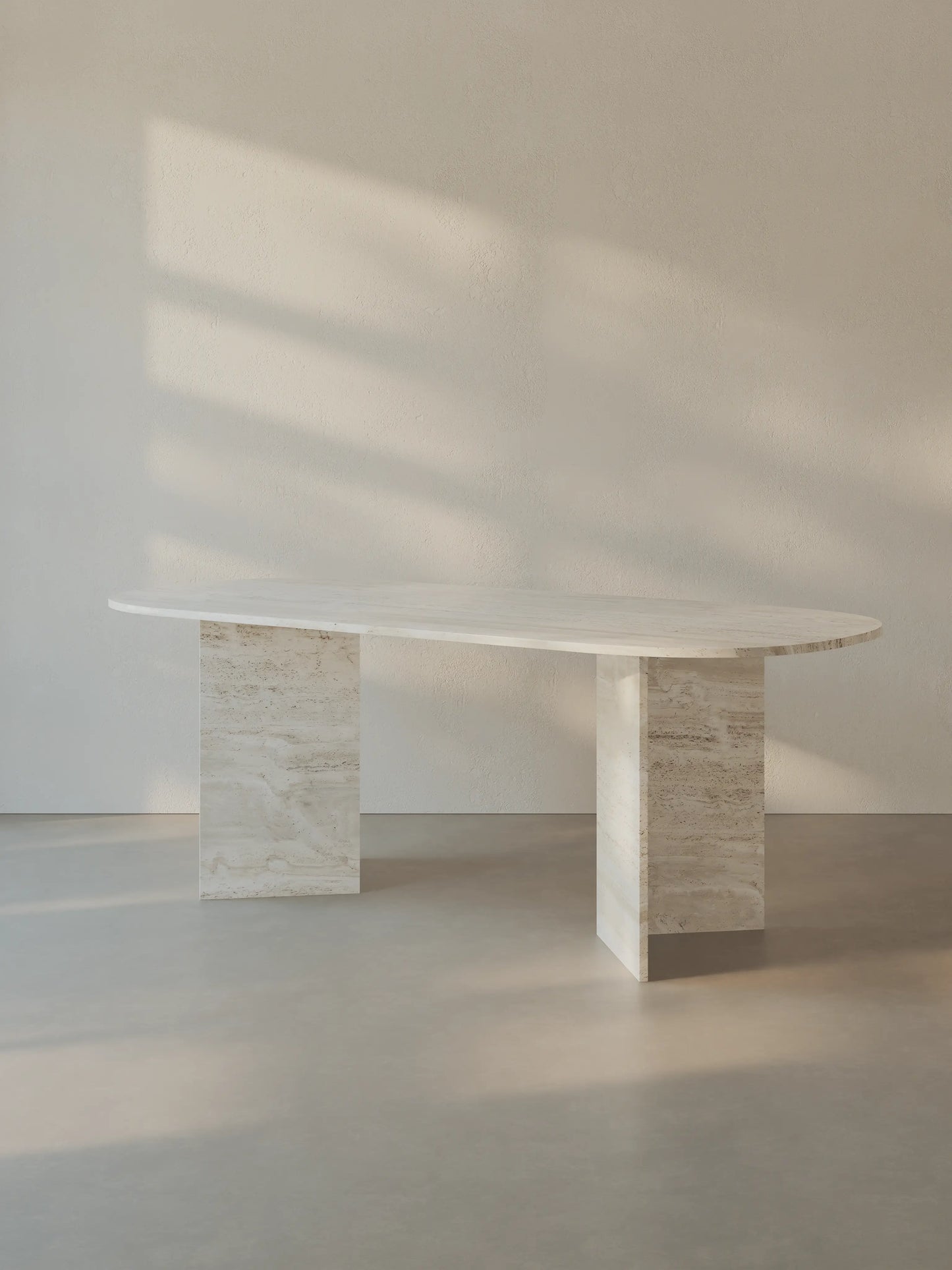 Sienae Dining Table in Navona Travertine with oval-edged tabletop, shown from a slight angle highlighting the V-shaped base