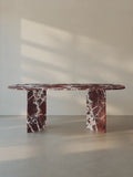 Sienae Dining Table in Rosso Levanto marble with oval-edged tabletop and sculptural V-shaped base, shown from the front