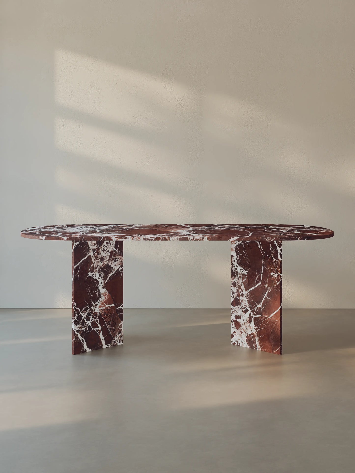 Sienae Dining Table in Rosso Levanto marble with oval-edged tabletop and sculptural V-shaped base, shown from the front