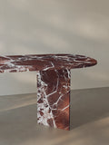 Side view of the Sienae Dining Table in Rosso Levanto marble showing the sculptural V-shaped base