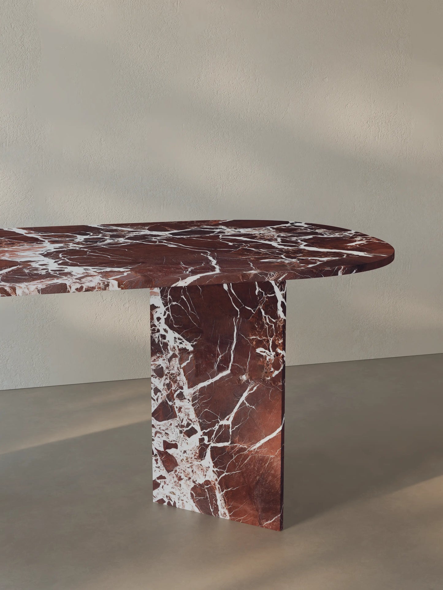 Side view of the Sienae Dining Table in Rosso Levanto marble showing the sculptural V-shaped base