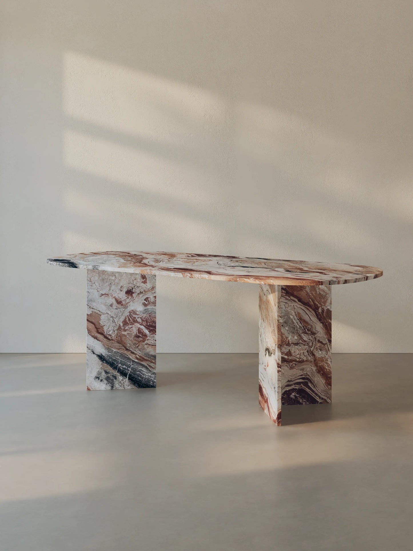 Sienae Dining Table in Rosso Orobico marble with oval-edged tabletop, shown from a slight angle highlighting the V-shaped base