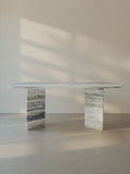 Sienae Dining Table in Silver Travertine with oval-edged tabletop and sculptural V-shaped base, shown from the front.