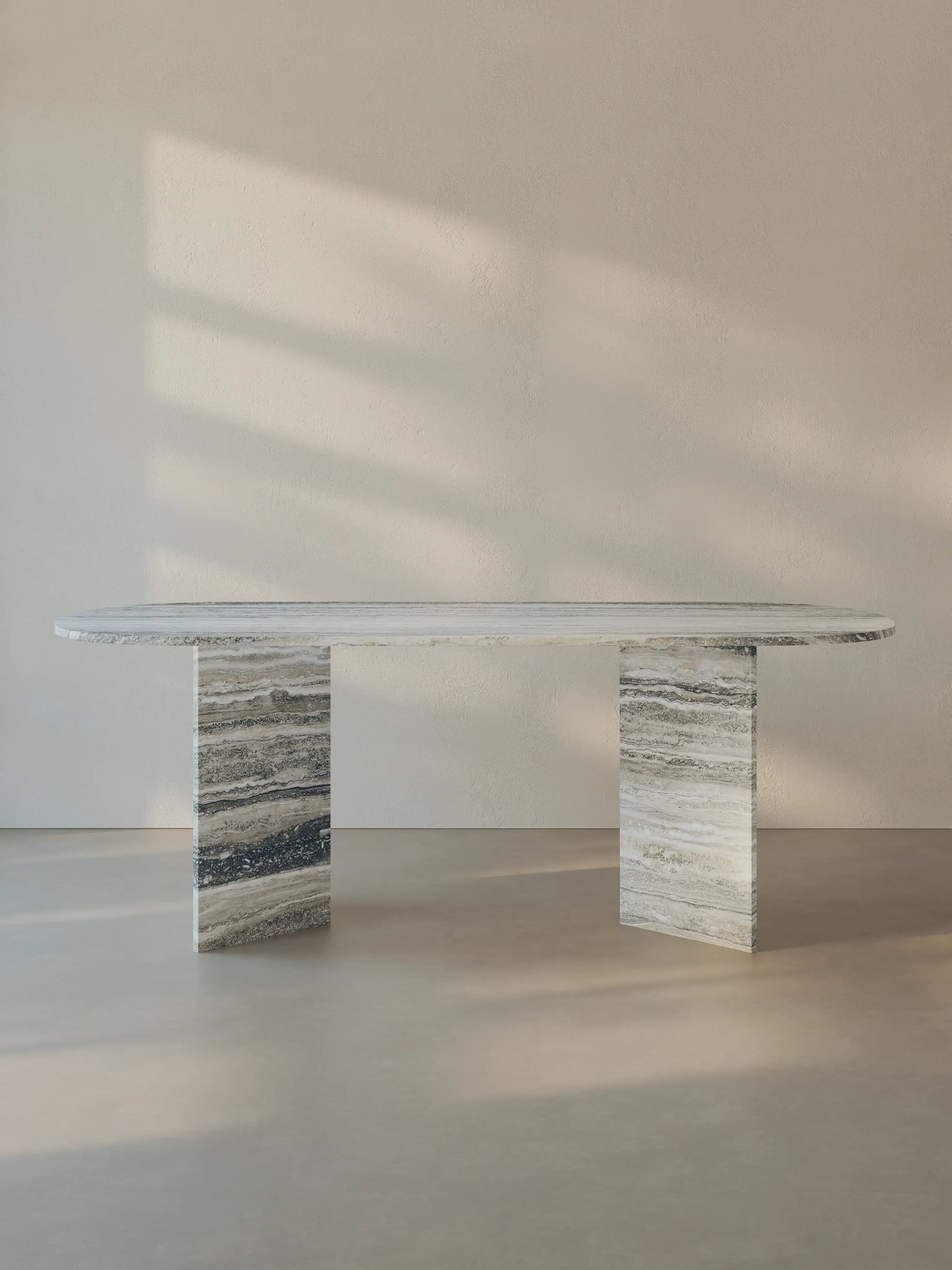 Sienae Dining Table in Silver Travertine with oval-edged tabletop and sculptural V-shaped base, shown from the front.