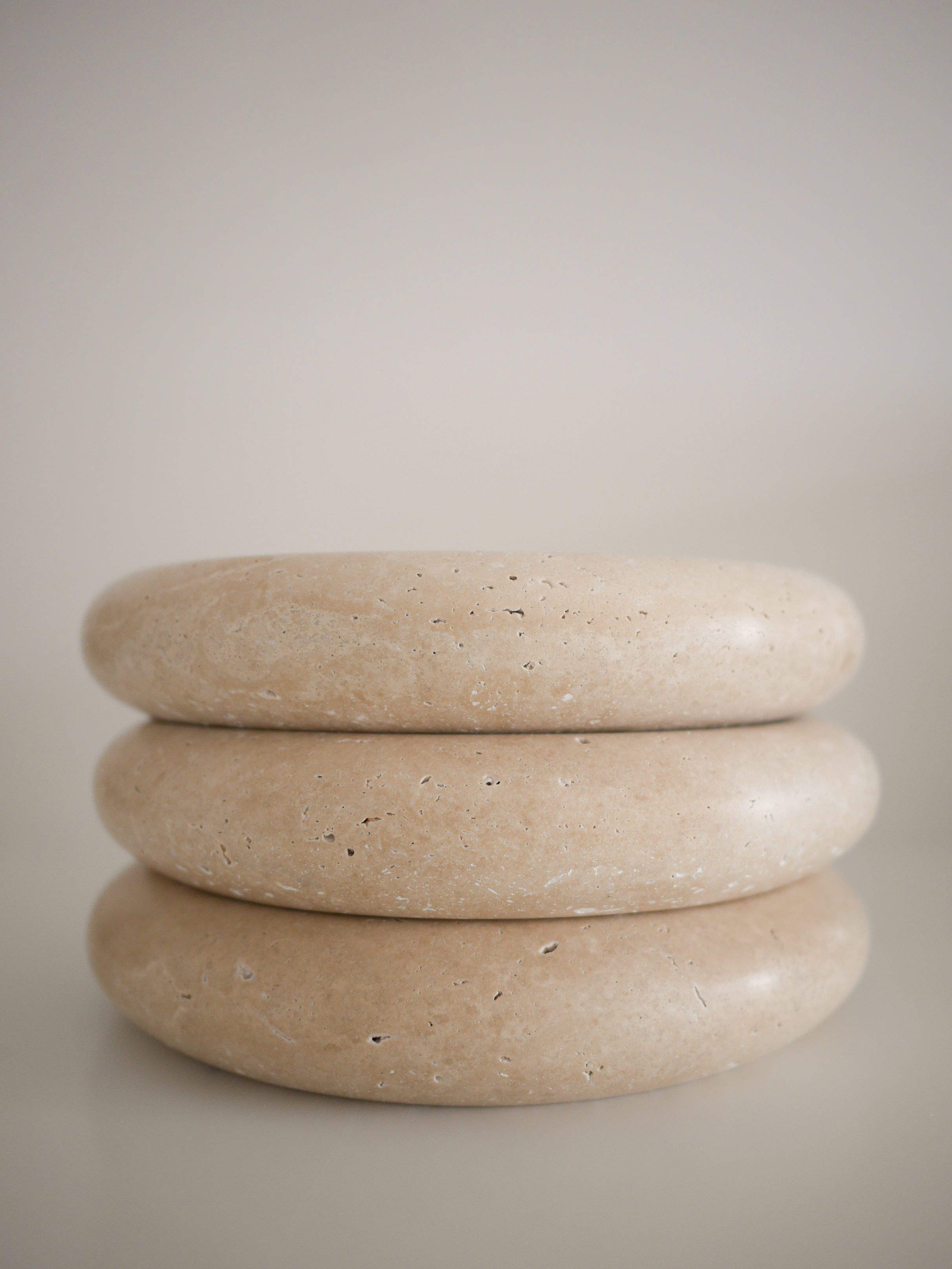 Three Flat Fata travertine dishes stacked atop one another, highlighting their refined, rounded form and the organic texture of natural stone.