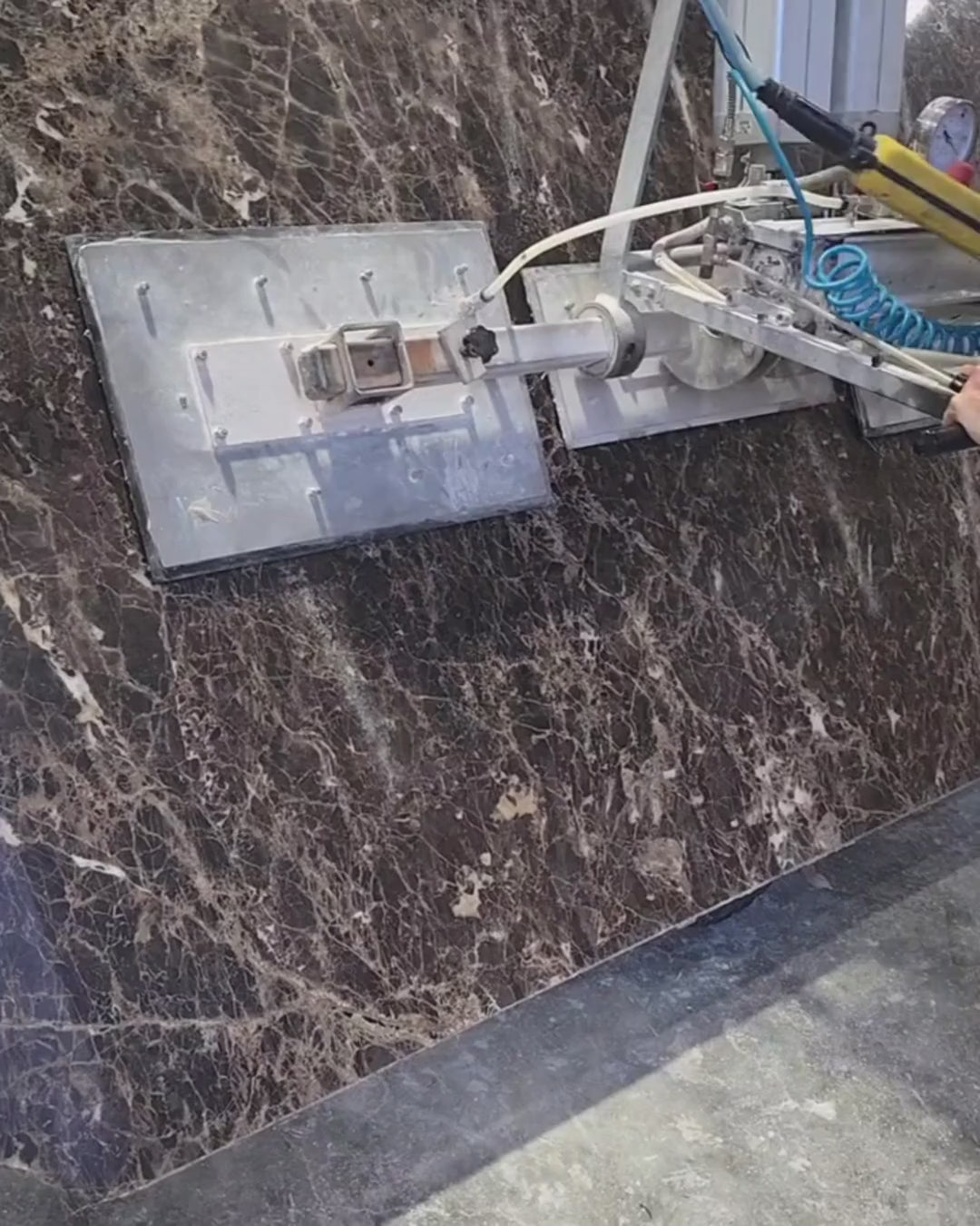Dark Emperador marble slab being lifted and positioned inside the workshop